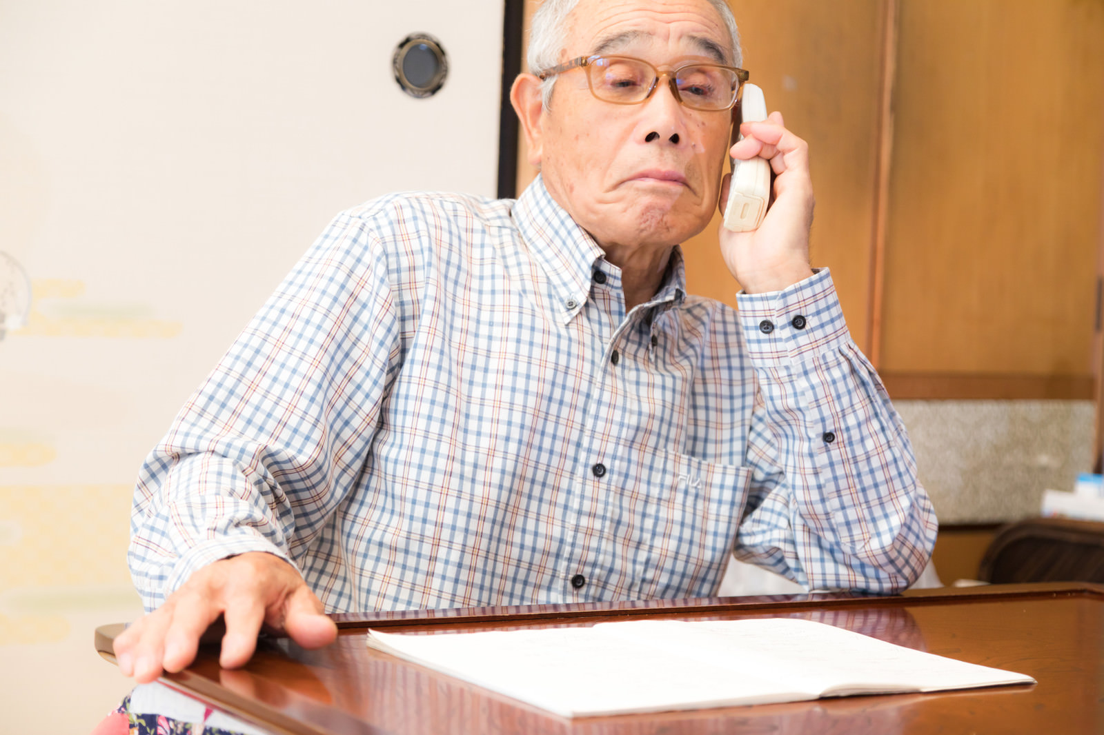 自宅で電話をしながら書類を確認する高齢者の写真